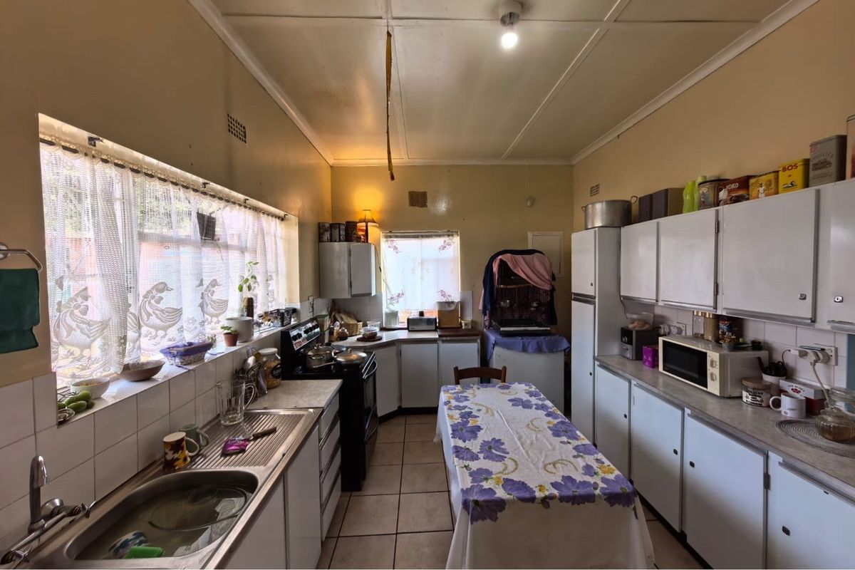 A functional kitchen featuring white cabinetry, tiled flooring, and a stainless steel sink, offering a traditional layout with ample natural light.