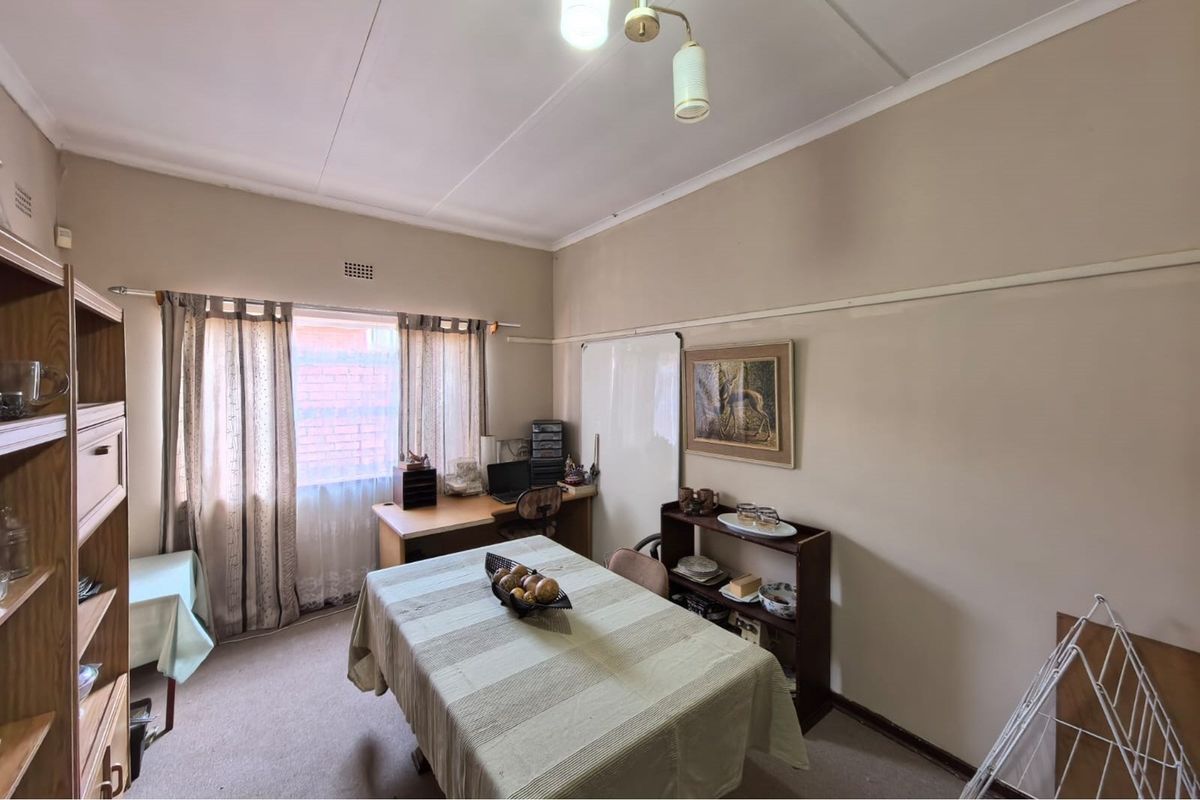 A functional bedroom or multi-purpose room featuring neutral walls, carpeted flooring, and a window with curtain tracks.