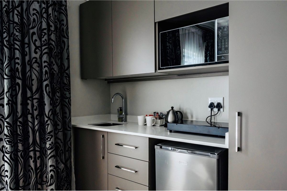 Compact kitchenette featuring modern cabinetry, a built-in microwave, a sink with a chrome faucet, and a stone countertop.