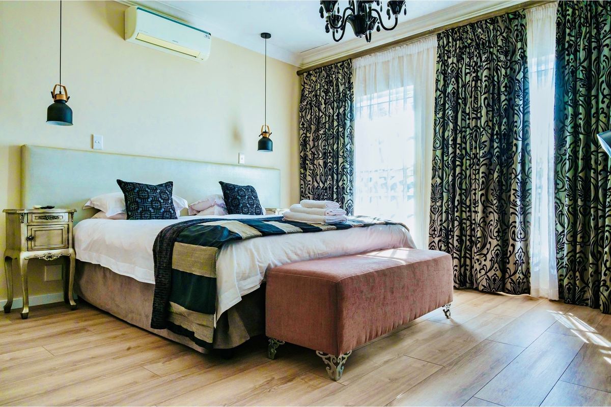 A well-appointed bedroom featuring wood-look flooring, a wall-mounted air conditioning unit, and floor-to-ceiling curtains leading to an outdoor area.