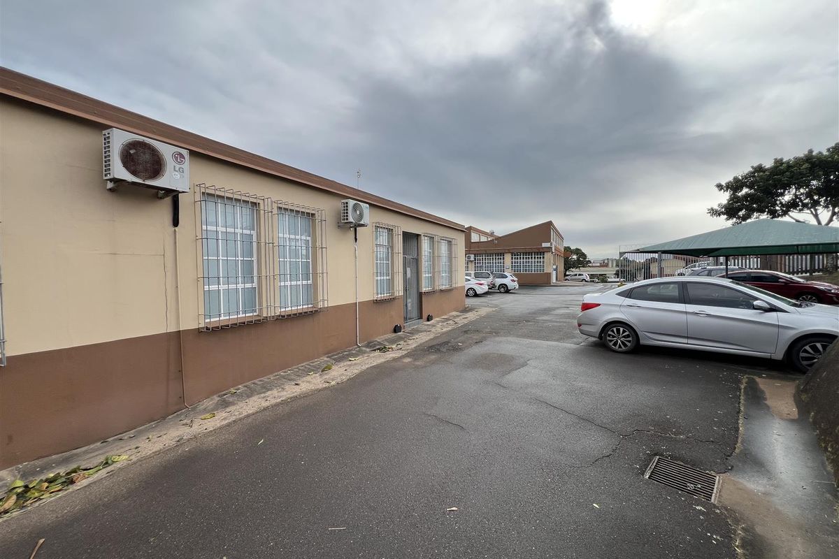 Exterior view of the industrial property featuring paved parking area, security bars on windows, and wall-mounted air conditioning units.