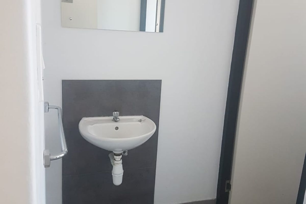 A functional industrial restroom featuring a wall-mounted basin with a tiled splashback, a mirror, and a towel rail.