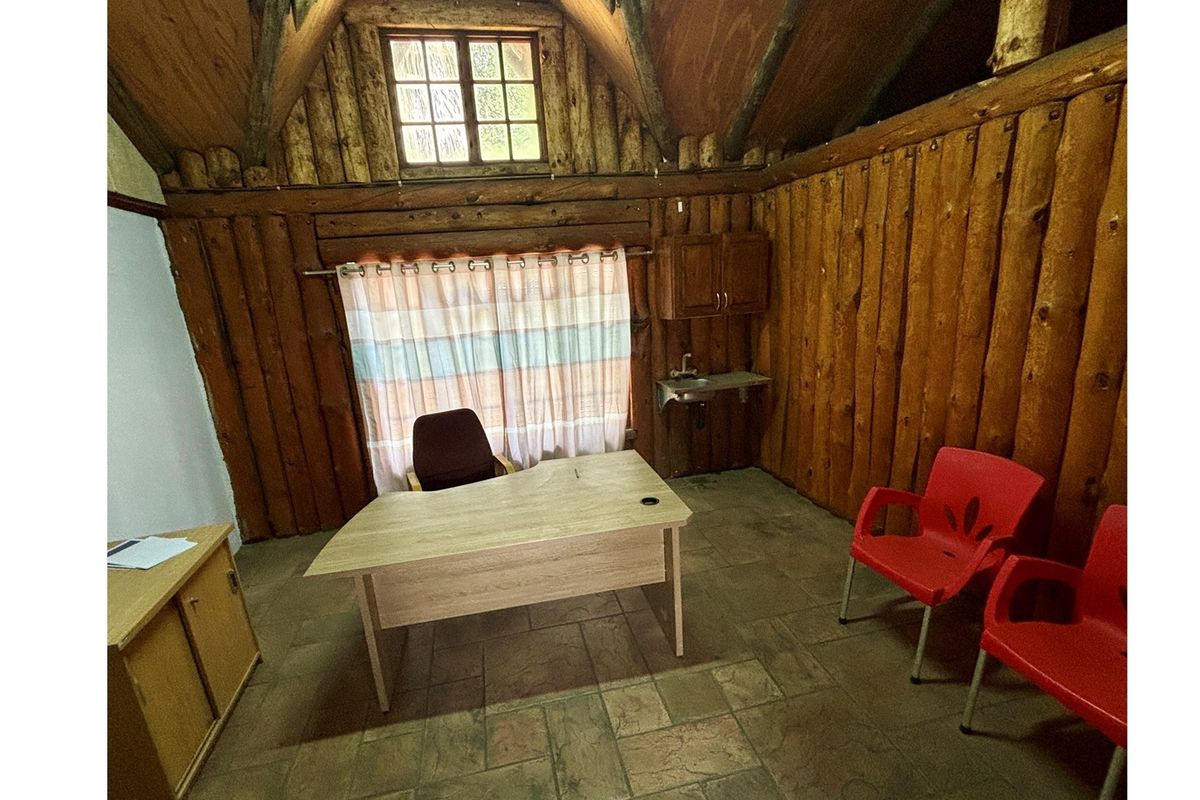 Rustic office space featuring log wall cladding, exposed timber rafters, tiled flooring, and a small wall-mounted sink with overhead cabinetry.