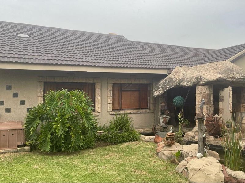 Front exterior view of the house featuring a tiled roof, stone-clad entrance detail, and a landscaped garden area with a small pond.