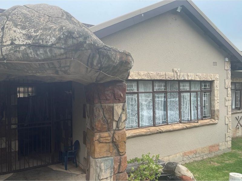 Front elevation of a house featuring unique rock-style stone cladding, metal security bars on windows, and a covered entrance area.