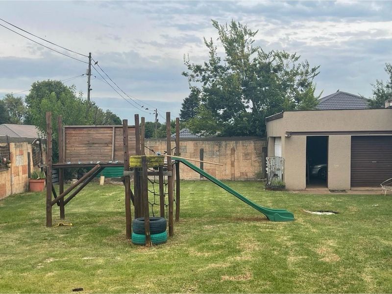 A spacious rear garden featuring a lawn area, a detached garage, and a perimeter boundary wall.