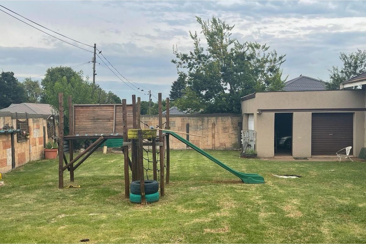 A spacious rear garden featuring a lawn area, a detached garage, and a perimeter boundary wall.