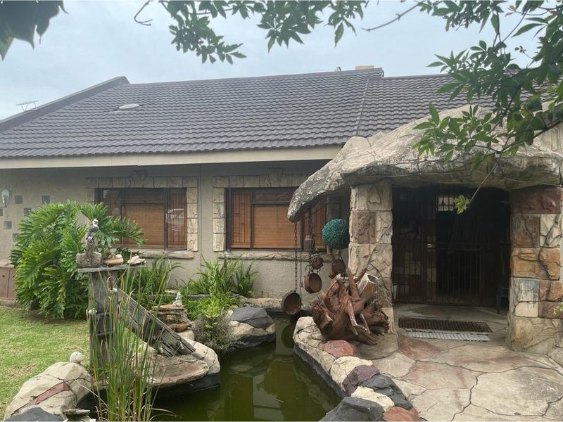 Front exterior view of the house featuring a tiled roof, stone-clad entrance porch, and a decorative garden pond.