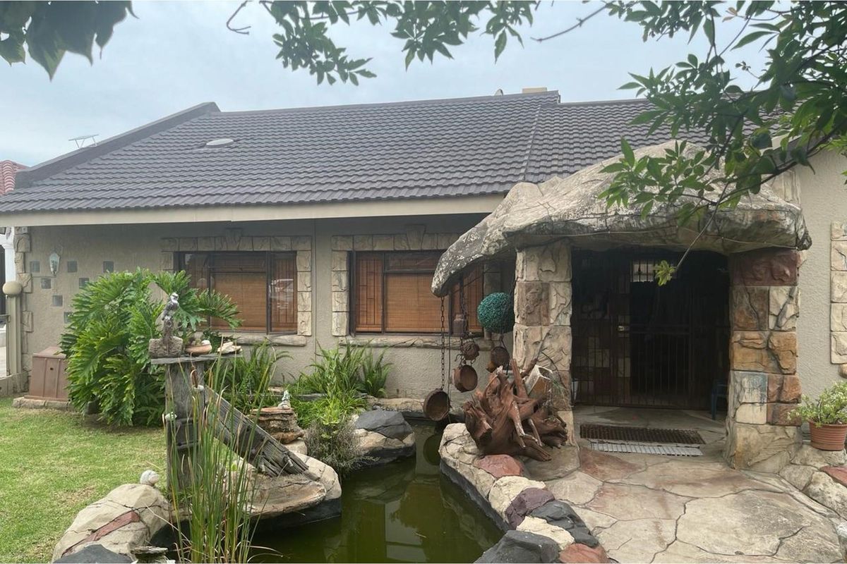 Front exterior view of the house featuring a tiled roof, stone-clad entrance porch, and a decorative garden pond.