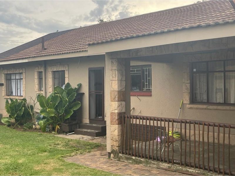A rear view of the house featuring a covered patio area, stone-clad pillars, tiled roof, and a small garden space.