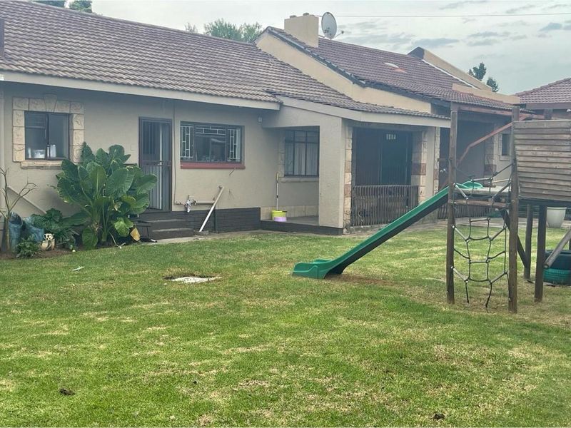 Rear view of the house featuring a tiled roof, covered patio area, and a spacious garden with a children's play structure.
