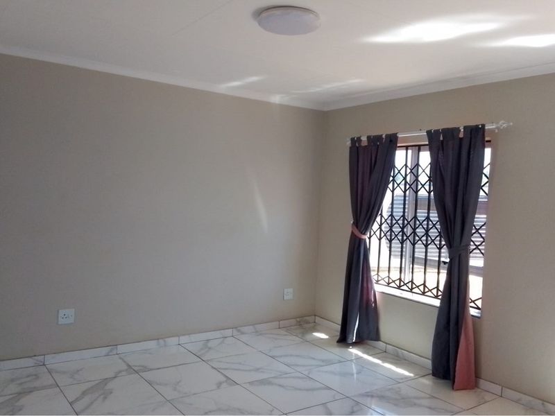 A bright, empty living room featuring modern marble-look floor tiles, neutral wall paint, and a secure window with a fitted security gate.