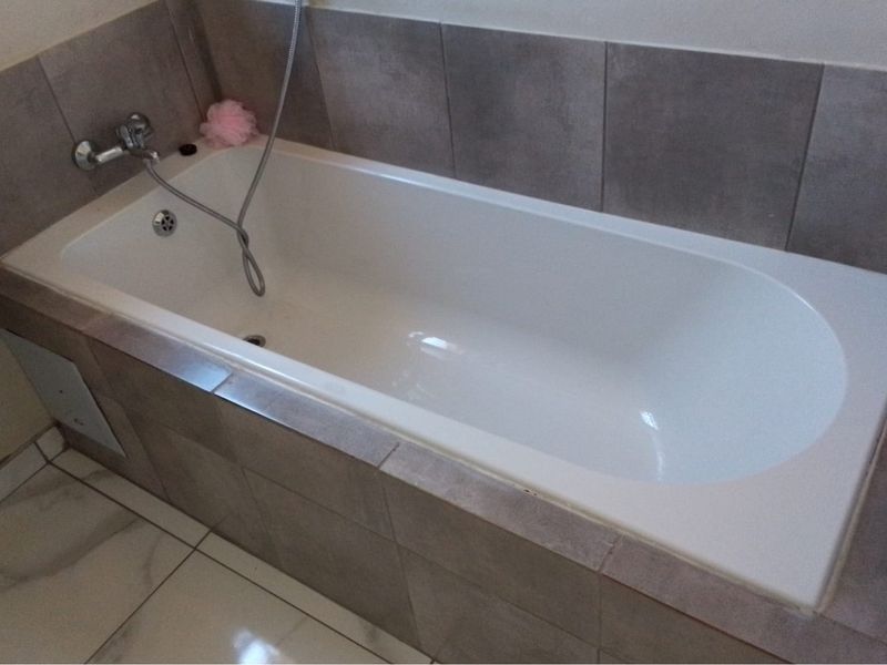 A functional bathroom featuring a built-in bathtub with wall-mounted mixer tap, complemented by neutral ceramic wall and floor tiling.