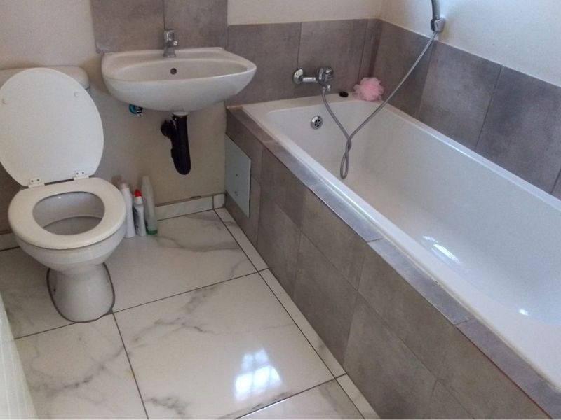 A functional bathroom featuring a bathtub with handheld shower mixer, wall-mounted basin, and tiled finishes throughout.