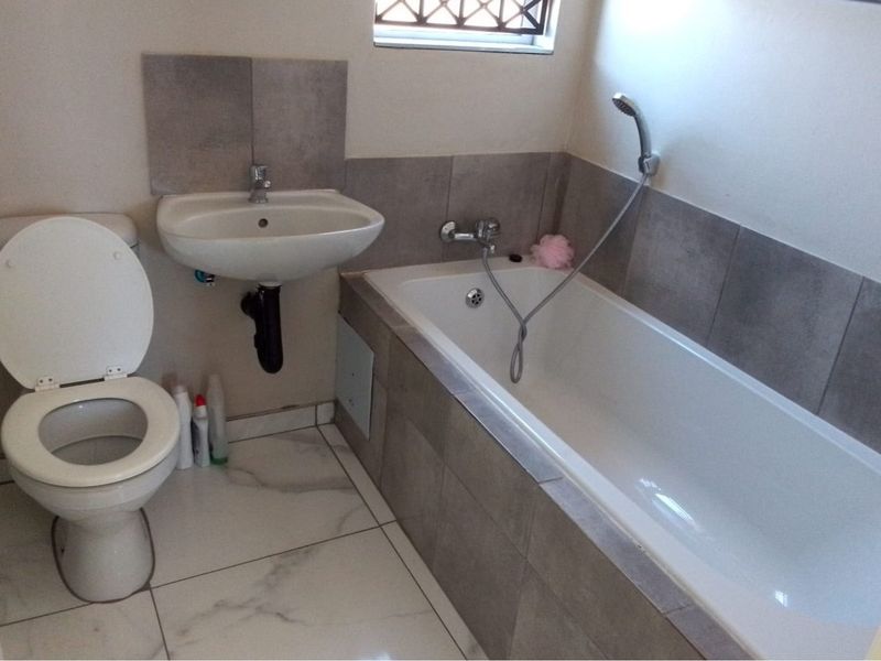 A clean, functional bathroom featuring a wall-mounted basin, a standard toilet, and a bathtub with a handheld shower mixer, finished with modern grey tiling.