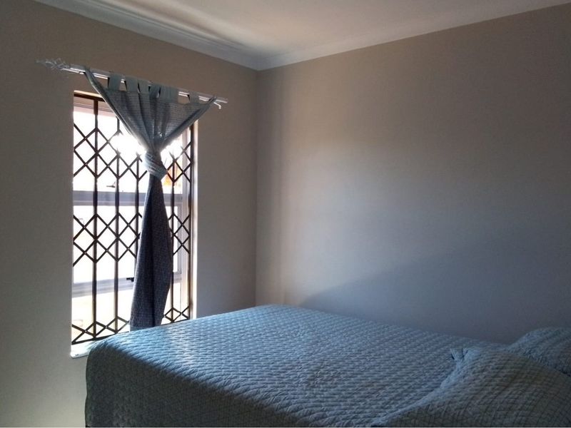 A simple bedroom featuring a window with a fitted security gate and neutral wall finishes.