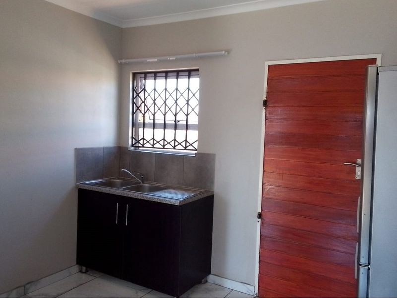 A functional scullery area featuring a stainless steel double sink, tiled splashback, built-in base cabinetry, and tiled flooring.