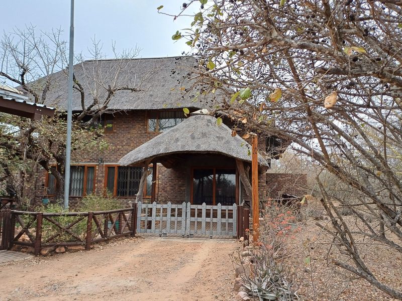 Front view of a rustic face brick house featuring a traditional thatched roof, timber entrance gate, and sliding glass doors.
