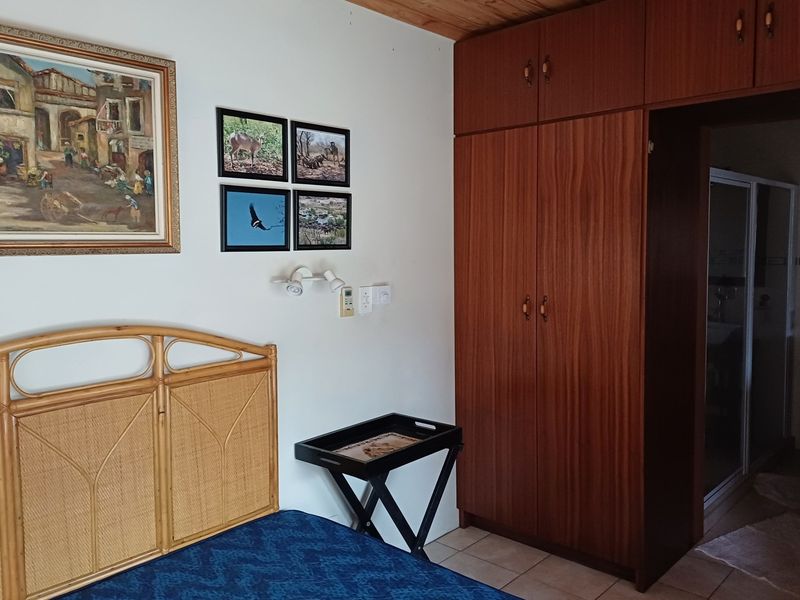 A bedroom featuring built-in wooden wardrobes, tiled flooring, and a timber ceiling, with an adjoining bathroom visible through the doorway.