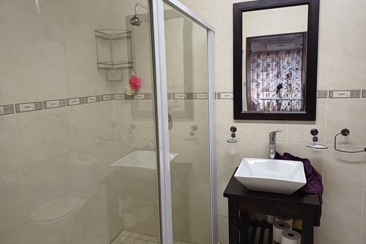 A functional bathroom featuring a glass shower enclosure, a modern vessel sink on a vanity cabinet, and neutral wall tiling.