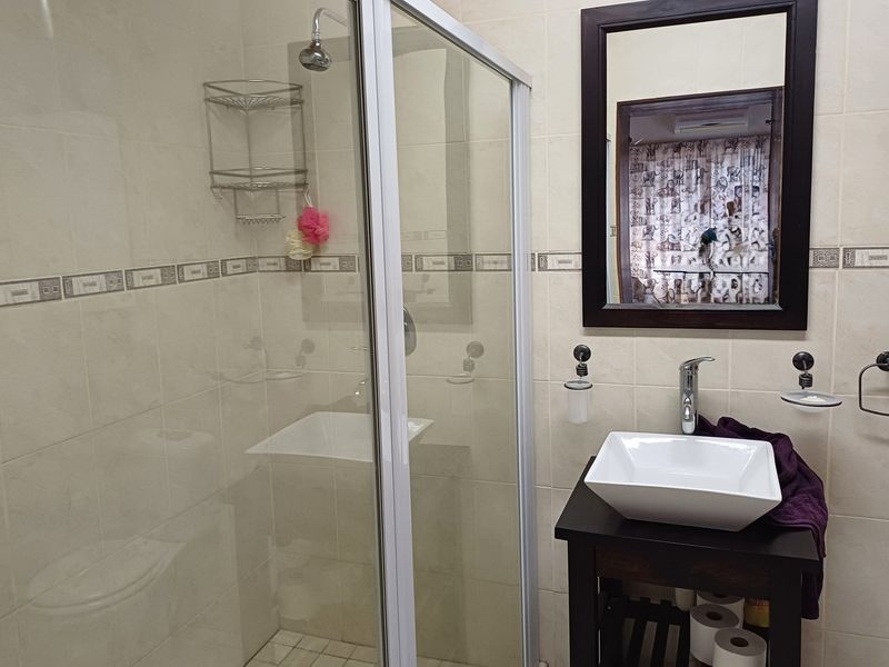 A functional bathroom featuring a glass shower enclosure, a modern vessel sink on a vanity cabinet, and neutral wall tiling.