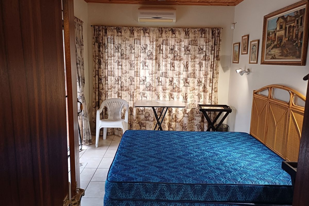 A bedroom featuring tiled flooring, a timber ceiling, and a wall-mounted air conditioning unit, offering a functional space with neutral finishes.