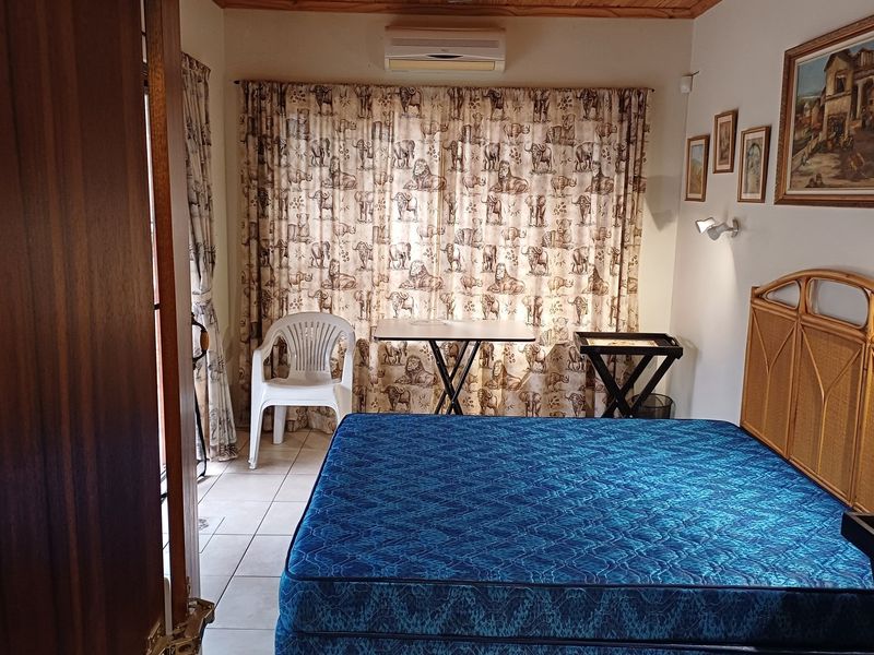 A bedroom featuring tiled flooring, a timber ceiling, and a wall-mounted air conditioning unit, offering a functional space with neutral finishes.
