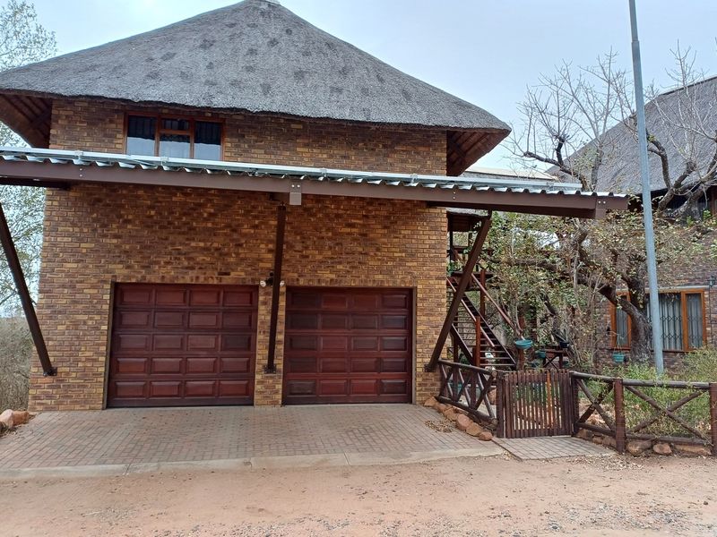 A double garage with a thatched roof and facebrick facade, featuring a paved driveway and an external timber staircase leading to the upper level.
