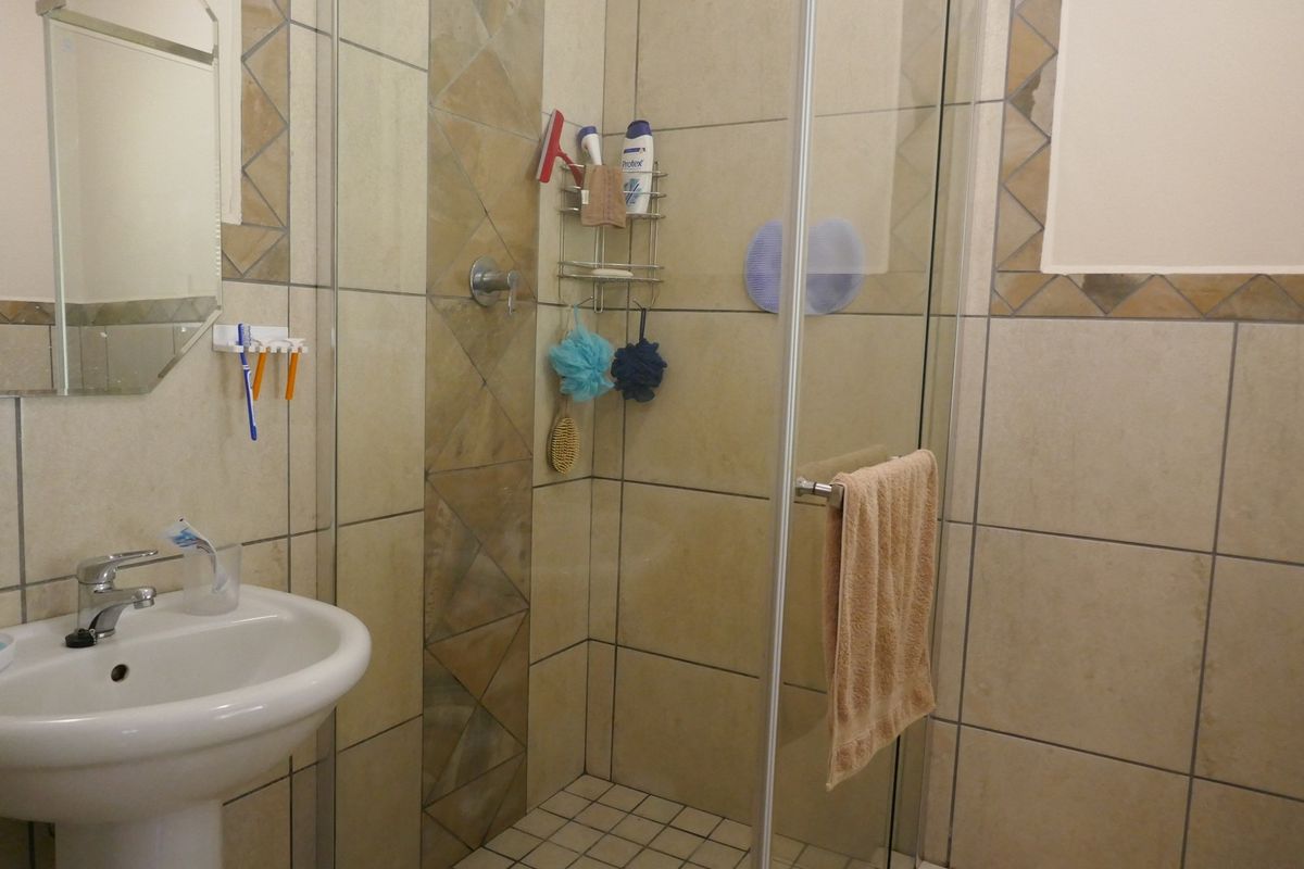 A functional bathroom featuring a pedestal basin, a glass-enclosed shower, and neutral wall tiling with decorative accent borders.