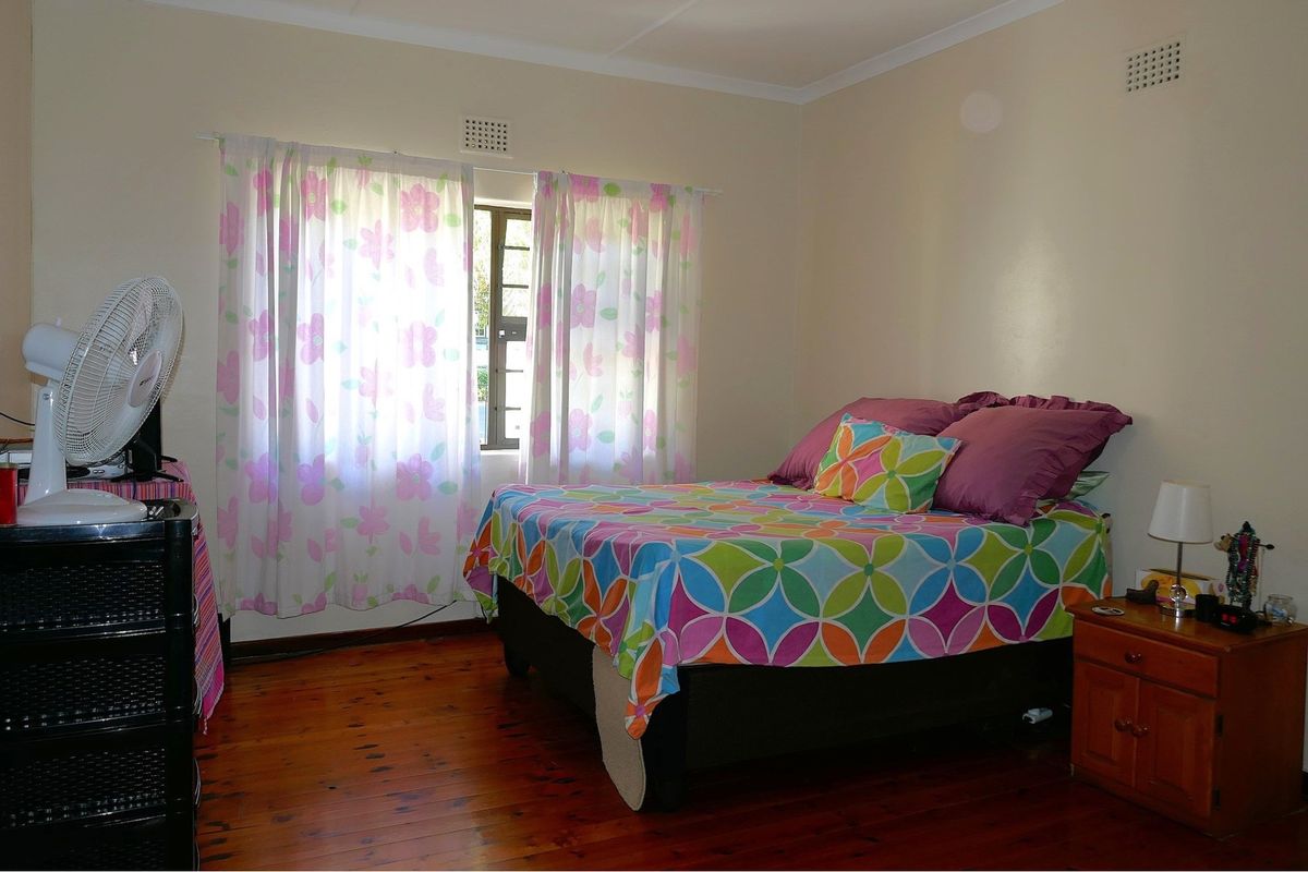 A bedroom featuring polished timber flooring and natural light from a window with curtain fixtures.