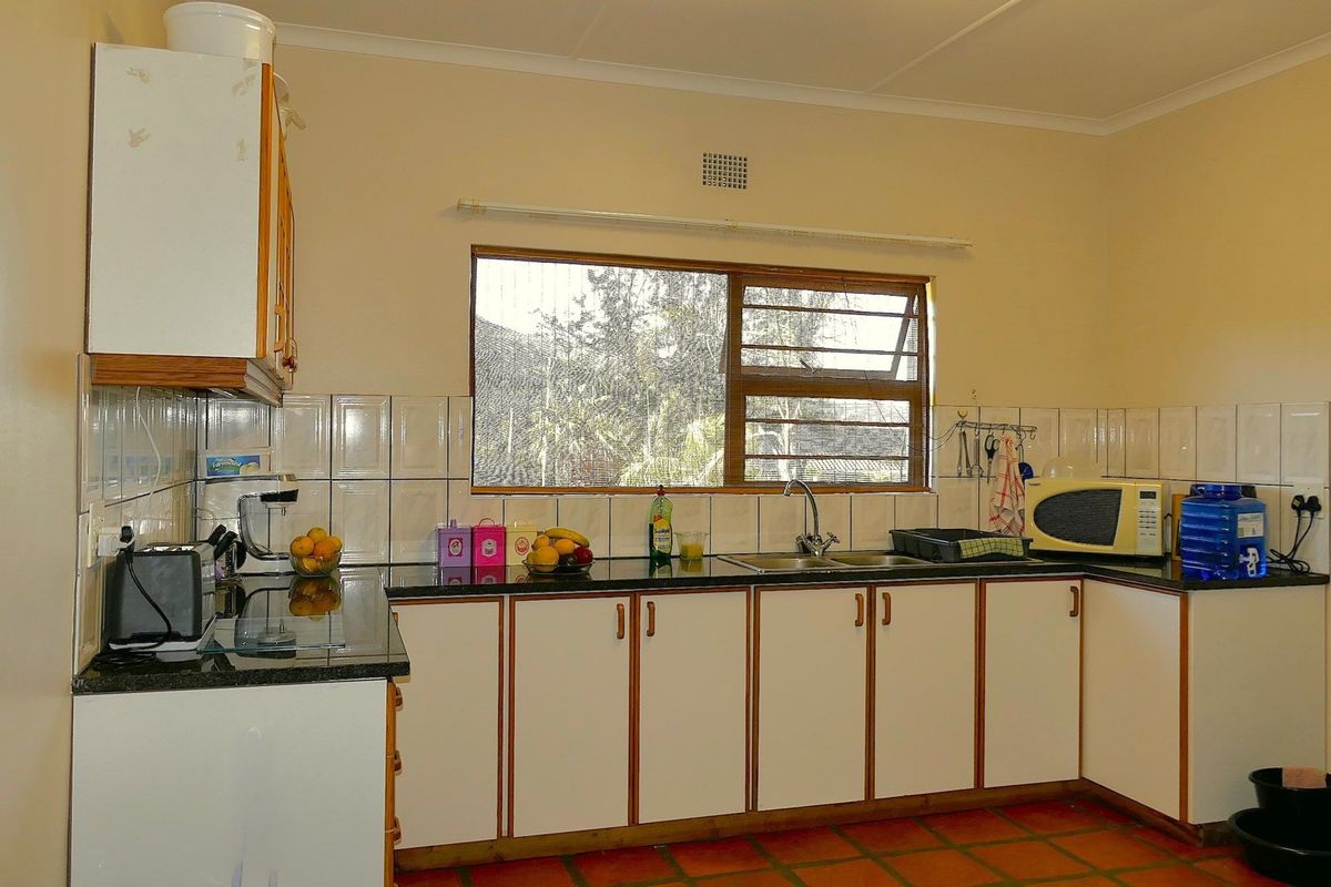 Functional kitchen featuring dark granite countertops, white cabinetry with wood trim, stainless steel sink, and large window providing natural light.