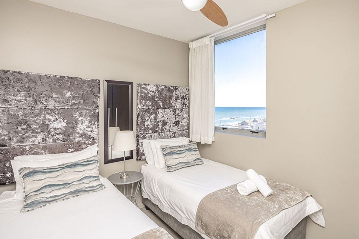 A bright bedroom featuring twin beds, wall-mounted headboards, and a large window offering scenic ocean views.