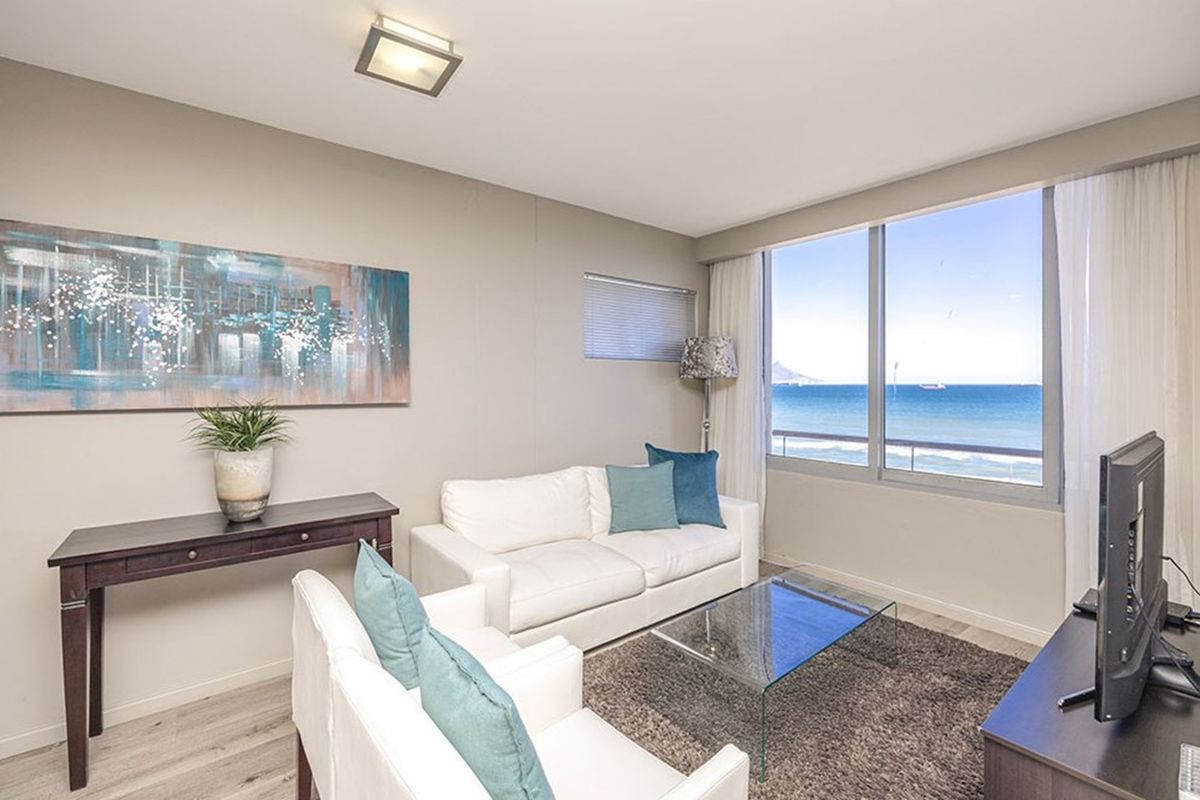 A bright living room featuring large windows with expansive ocean views, neutral wall tones, and modern laminate flooring.