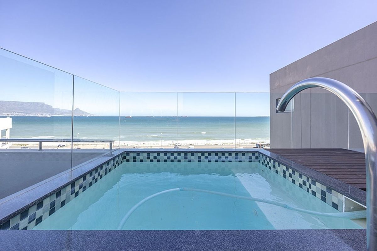 A private rooftop plunge pool featuring a glass balustrade, granite coping, and panoramic ocean and mountain views.