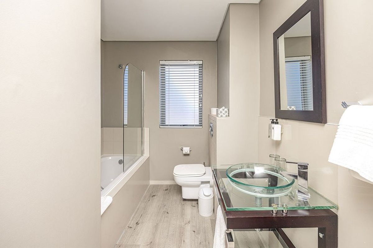 A modern bathroom featuring a glass vessel sink, a bathtub with a glass shower screen, and a wall-mounted toilet.