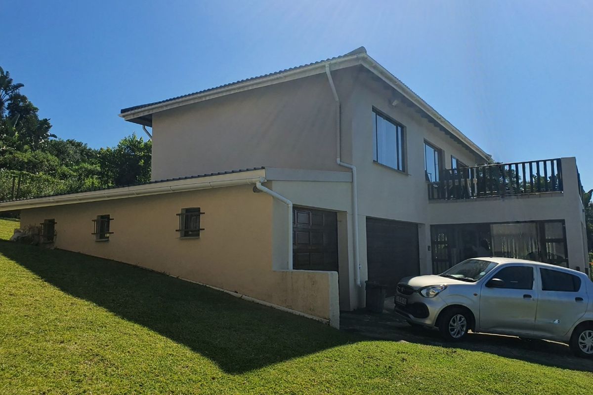 Side and rear view of a two-story residential house featuring a garage, balcony, and sloped lawn area.
