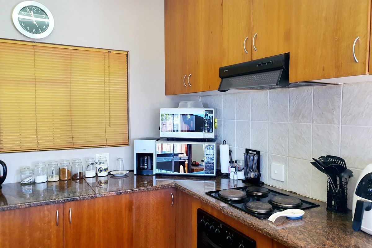 A functional kitchen featuring wood-veneer cabinetry, granite countertops, a built-in electric hob, and an extractor fan with a tiled backsplash.