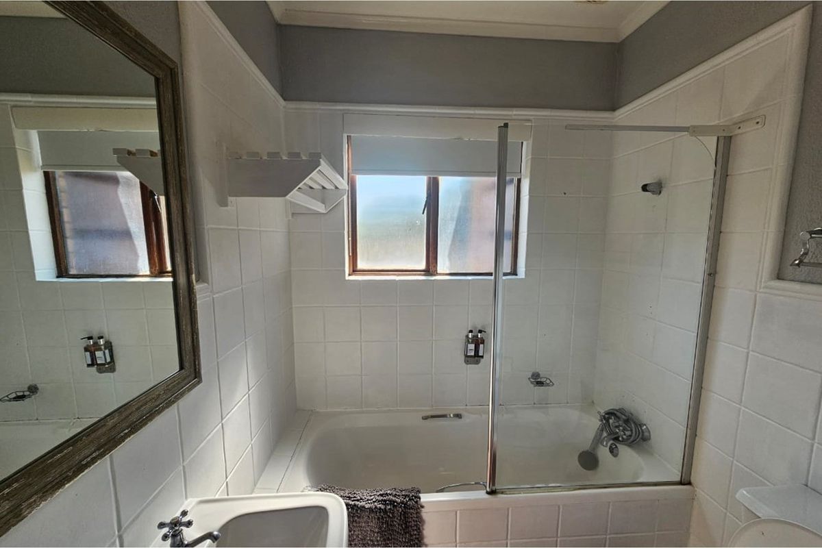 A functional bathroom featuring a built-in bathtub with a glass shower screen, wall-mounted basin, and tiled splashbacks.