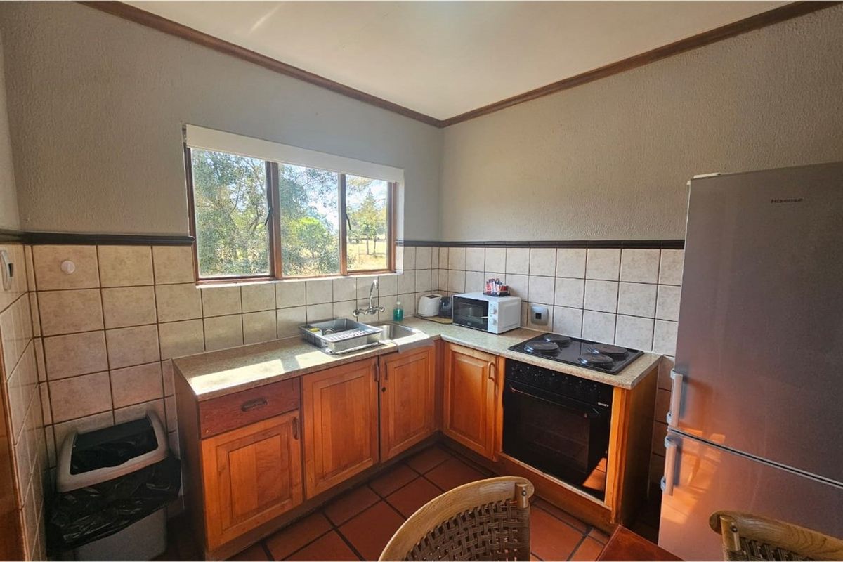 A functional kitchen featuring wooden cabinetry, a built-in oven with electric hob, tiled backsplash, and a window overlooking the garden.