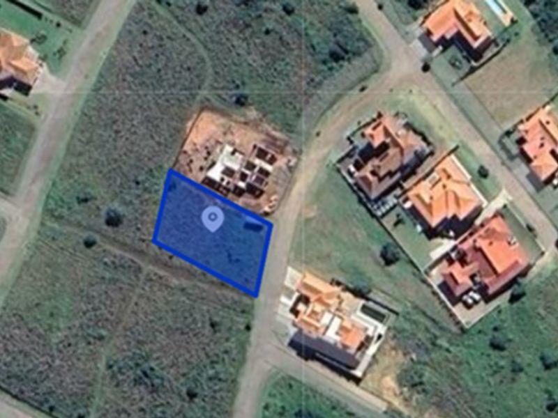 An aerial view of a vacant residential land plot highlighted in blue, situated within a developed suburban estate.