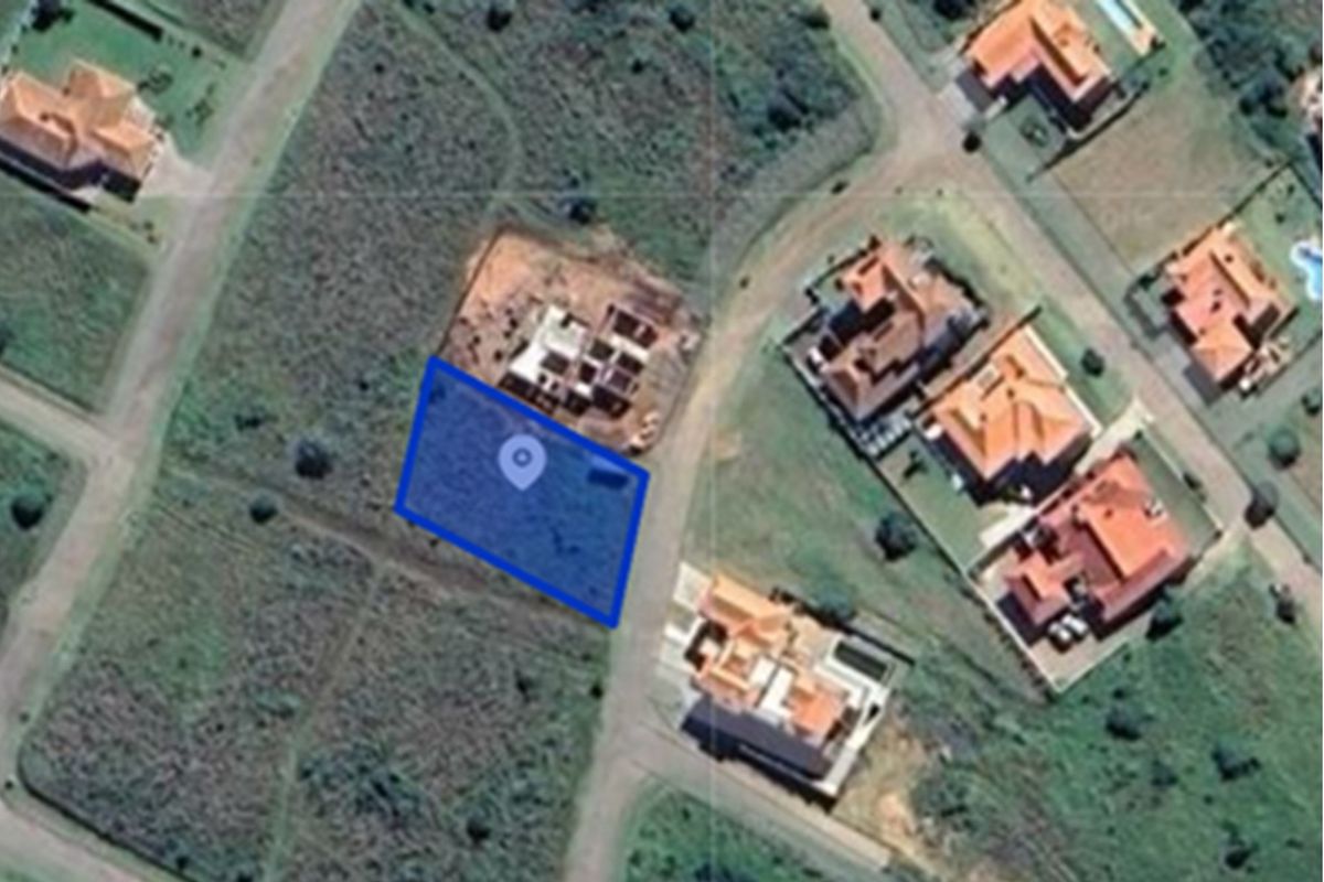 An aerial view of a vacant residential land plot highlighted in blue, situated within a developed suburban estate.