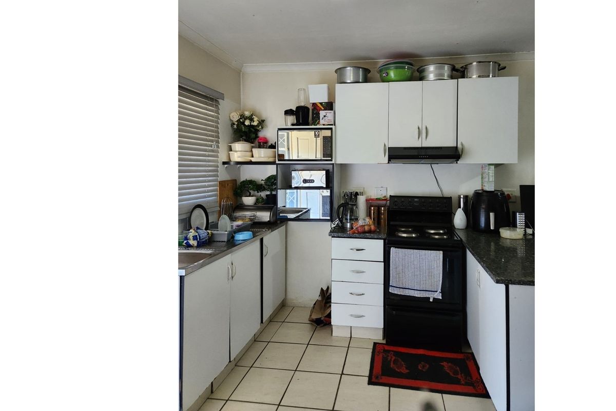 Compact kitchen featuring white cabinetry, granite-look countertops, a freestanding stove with extractor fan, and tiled flooring.