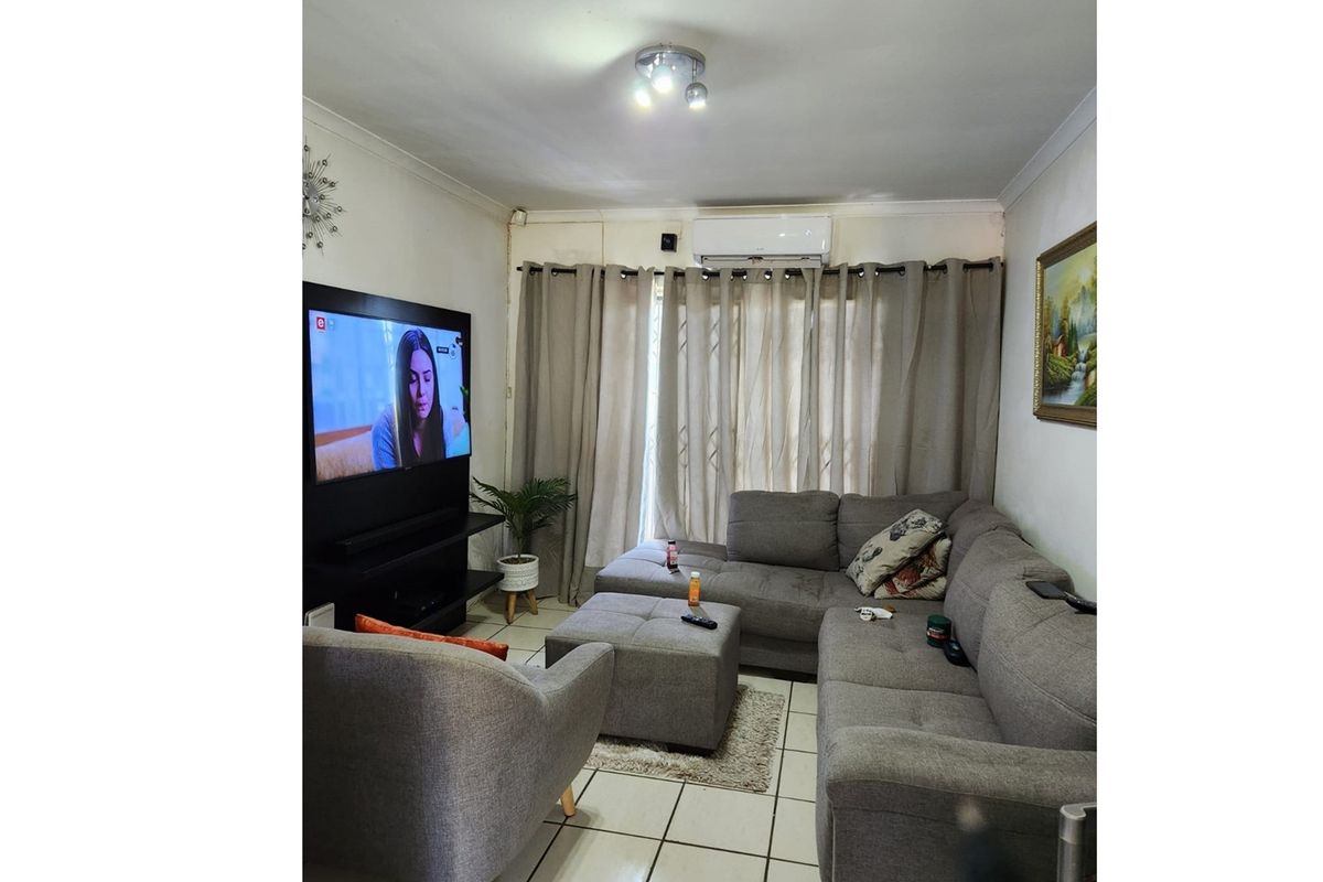 A cozy living room featuring tiled flooring, a wall-mounted air conditioning unit, and large windows dressed with curtains.