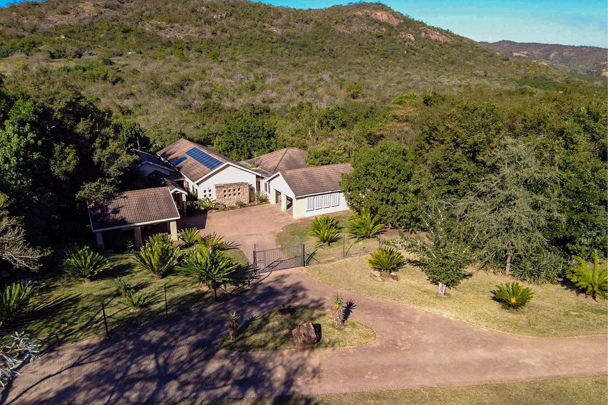 Aerial view of a farm property featuring a main residence with tiled roofing, solar panels, and a paved driveway set within a lush landscape.