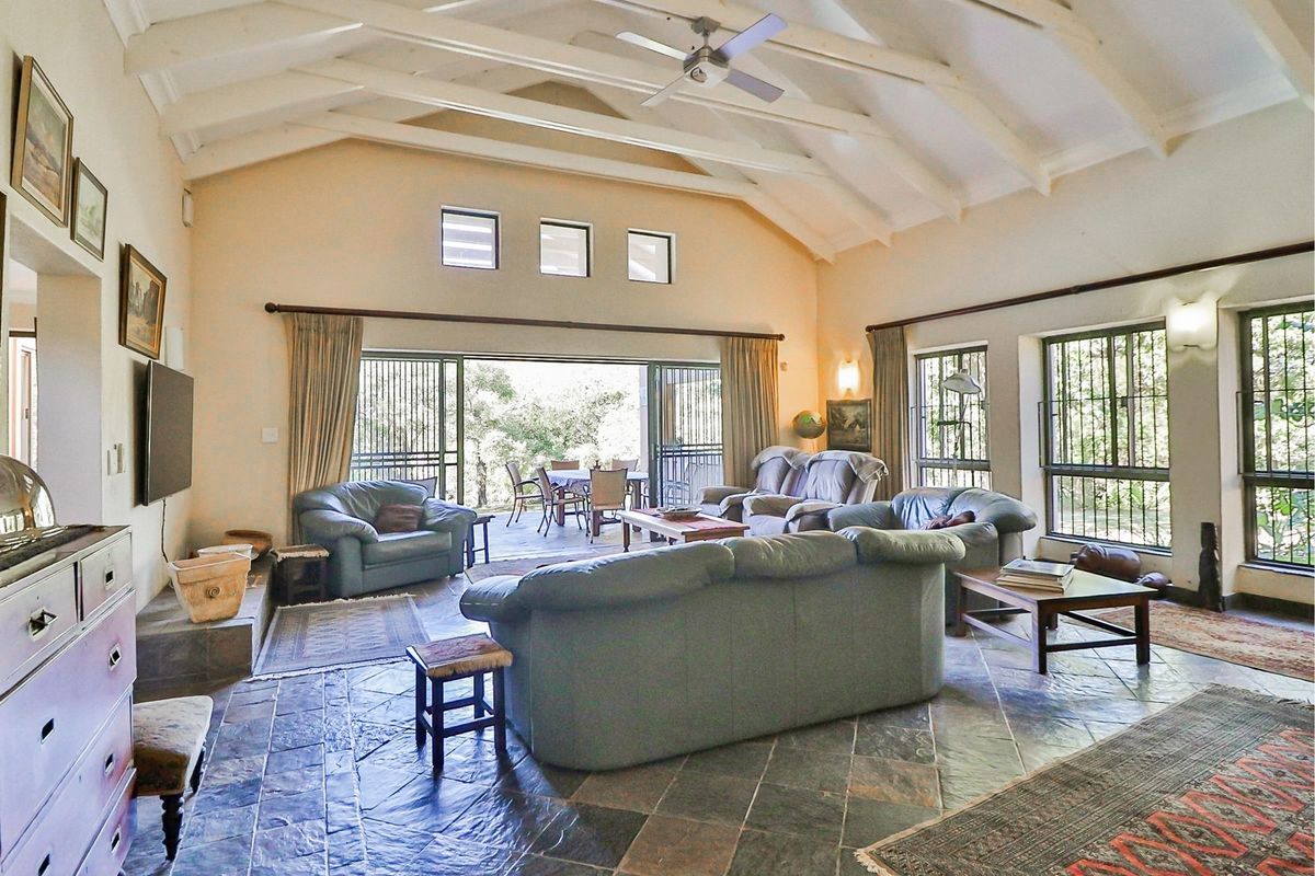 Spacious living room featuring vaulted ceilings with exposed beams, slate flooring, and large sliding doors opening onto a covered patio area.