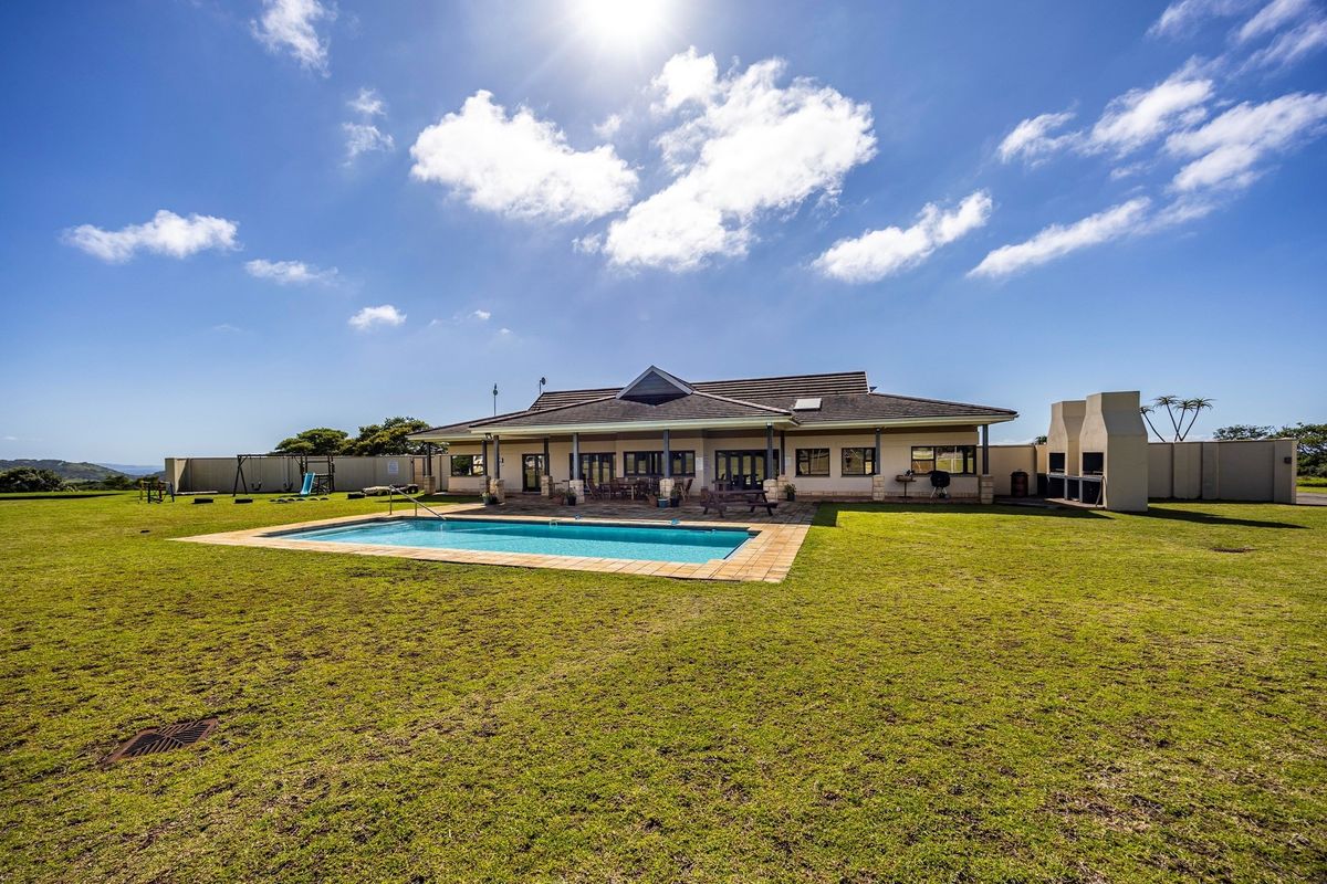 Spacious rear exterior view featuring a well-maintained swimming pool, expansive lawn, and a covered patio area attached to the main residence.