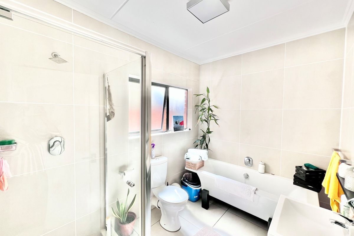 A bright, modern bathroom featuring a glass-enclosed shower, a separate bathtub, a toilet, and neutral wall tiling.