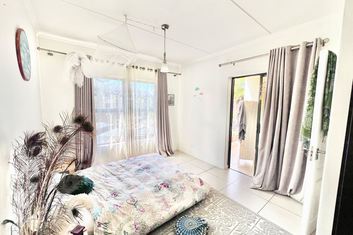 A bright bedroom featuring tiled flooring, large windows, and a sliding glass door providing direct access to an outdoor balcony area.