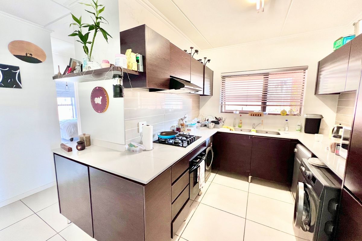 A functional kitchen featuring dark cabinetry, stone-look countertops, a built-in gas hob, extractor fan, and integrated laundry appliance space.