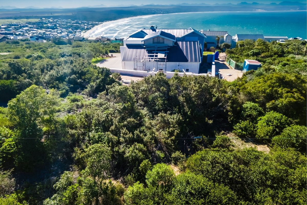 Aerial view of a residential property under construction, featuring coastal views and surrounding natural vegetation.